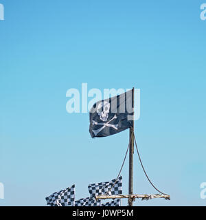 Il Teschio e Ossa Croce del tradizionale bandiera pirata conosciuto come il Jolly Roger volare alto contro un cielo blu Foto Stock