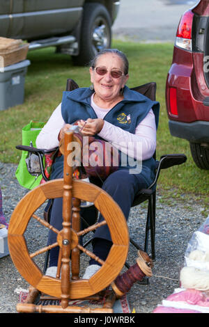 Un senior donna età rimanendo attivo partecipando nella sua città mercato di agricoltori con la sua ruota di filatura a Lisbona, New Hampshire, Stati Uniti. Foto Stock