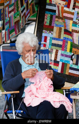 Un bianco con capelli donna senior gode di lavorazione a maglia di un maglione rosa presso il Mercato degli Agricoltori a Lisbona, New Hampshire, Stati Uniti. Foto Stock