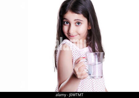 Bella felice bambina con lunghi capelli scuri e il vestito tenendo un bicchiere di acqua e guardando la fotocamera. studio shot, isolato su sfondo bianco. Foto Stock