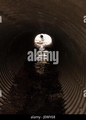 Guardando verso il basso una texture tunnel metallico nel giorno con luce riflessa nell'acqua proveniente attraverso con colori scuri e umore Foto Stock