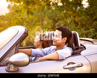 Giovane coppia asiatica di equitazione in una cabriolet auto sportive al tramonto. Foto Stock