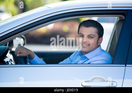 Closeup Ritratto, giovane uomo bello nel suo nuovo grigio argento auto, rilassante, mano sul volante, a guardare fuori dalla finestra, isolato su sfondo all'aperto Foto Stock