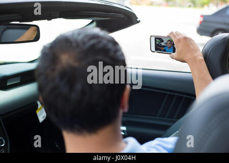 Closeup ritratto, happy fun giovane azienda telefono sta immagine di sé nel nuovo di zecca auto sportiva, isolata all'esterno al di fuori di sfondo Foto Stock