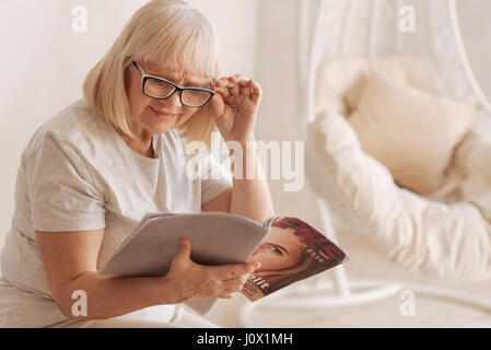 Piacevole di età donna leggendo una rivista di moda Foto Stock