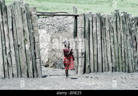 Un giovane bambino Masai al di fuori del villaggio recintato Foto Stock