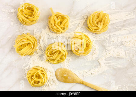 Una foto aerea di nidi di pasta su un bianco tavola di marmo con farina e con un mestolo di legno e un posto per il testo Foto Stock