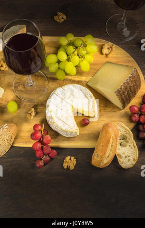 Una foto di una selezione di formaggi a una degustazione di vino e in abbinamento con pane, viola e uve bianche, noci e bicchieri Foto Stock