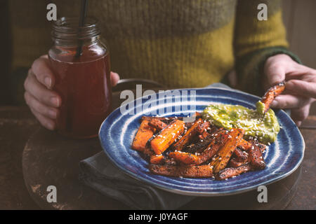 Donna di mangiare carote arrosto con salsa di avocado in orizzontale Foto Stock