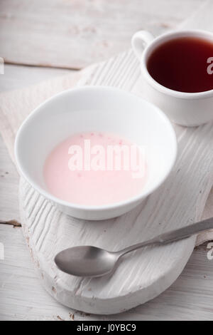Yogurt alla frutta e la tazza di tè sul bianco tavolo in legno Foto Stock