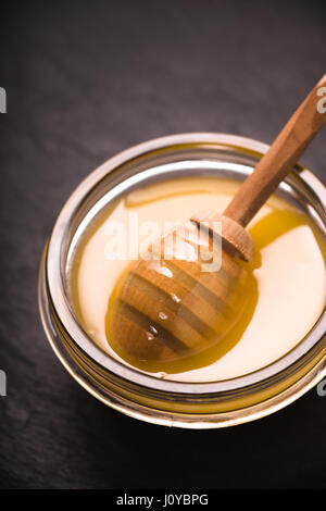 Versare in una ciotola di miele al buio su un primo piano di ardesia Foto Stock