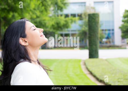 Closeup Ritratto, giovane donna in maglia bianca la respirazione nella fresca aria fresca dopo una lunga giornata di lavoro, isolata all'esterno al di fuori dello sfondo. Arresto e odore Foto Stock