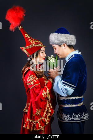 Coppia asiatica in nazionale costumi kazako tenendo i fiori e il profumo a sfondo grigio Foto Stock