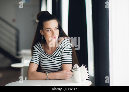 Ritratto di un adulto bella donna che guarda attraverso la finestra mentre si siede a un tavolo in una caffetteria. Foto Stock