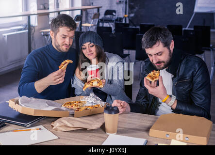 Il team Aziende di mangiare pizza e bere in ufficio Foto Stock