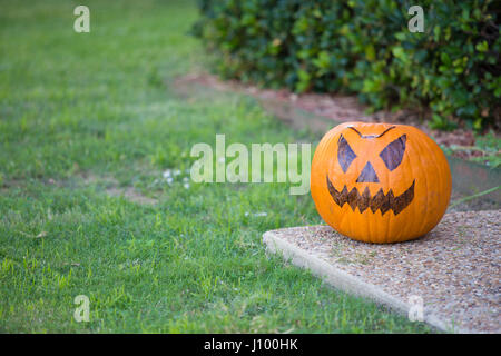 Closeup ritratto, arancione spaventoso halloween jack o'zucca lanterna seduta sul marciapiede, isolati alberi verdi e lo sfondo di erba. Il 31 ottobre trucco o Foto Stock