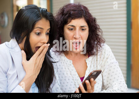 Closeup ritratto di due ragazze sorpreso guardando il telefono cellulare discutendo Ultime notizie news, shopping, molto meravigliato a ciò che vedono, isolata all'esterno Foto Stock