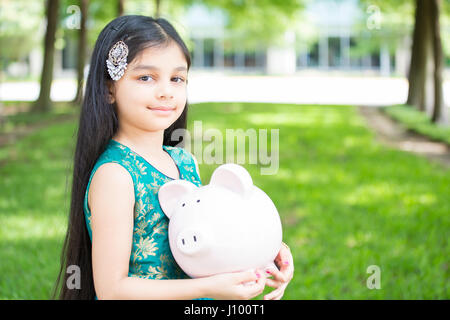 Closeup ritratto, signora giovane azienda salvadanaio, isolata all'esterno erba verde e alberi dello sfondo. Soldi strategia di costruzione Foto Stock