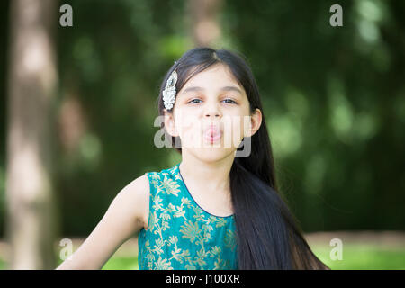 Closeup ritratto, ragazza giovane con la lingua fuori facendo facce buffe, isolato al di fuori all'aperto sullo sfondo Foto Stock