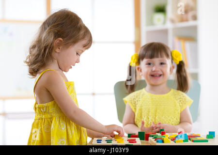 Ragazze Ragazzi giocare con il giocattolo logico sulla scrivania in nursery room o asilo nido. Disponendo i bambini e lo smistamento di forme, colori e dimensioni. Foto Stock