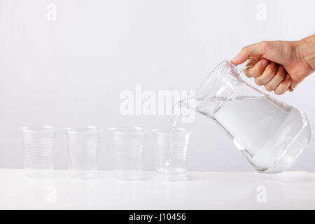 Mano versando acqua dalla caraffa di vetro di vetro contro uno sfondo bianco Foto Stock