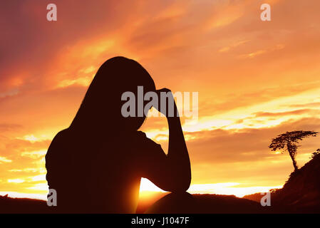 Premuto silhouette donna seduta da sola sulla cima di una montagna al tramonto Foto Stock
