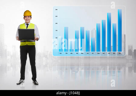 Giovane ingegnere asiatici Uomo con notebook in piedi accanto al reddito grafico su schermo digitale Foto Stock