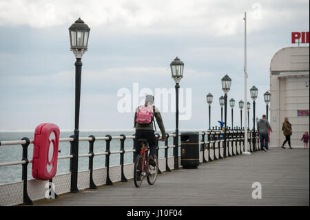 Worthing, West Sussex, Regno Unito. Un ciclista cavalca la sua bicicletta lungo Worthing Pier in un giorno nuvoloso. Foto Stock