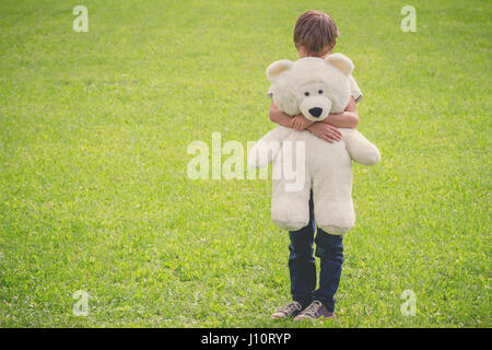 Triste ragazzo abbracciando il suo orsacchiotto di peluche Foto Stock