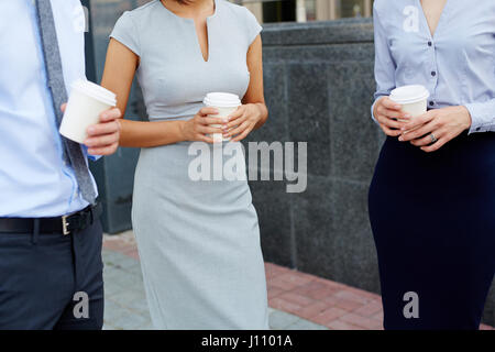 La sezione centrale shot, gruppo di gente di affari in piedi fuori ufficio moderno edificio parlando e tenendo la carta tazze da caffè Foto Stock
