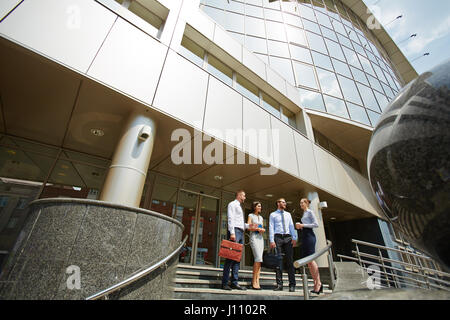 Ampia angolazione, gruppo di gente di affari in piedi sui gradini di un ufficio moderno edificio con facciate in vetro Foto Stock