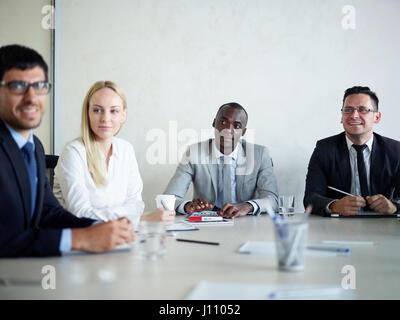 Multi-etnico gruppo di uomini di affari che incontro in sala conferenze: afro-americano di uomo seduto a tavola con i colleghi e sorridente Foto Stock