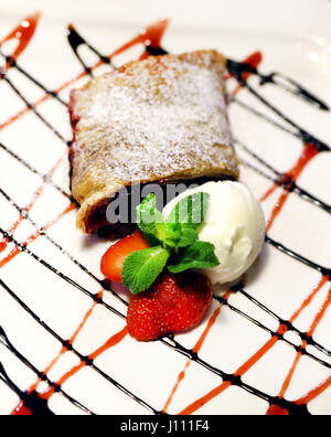 Un delizioso dessert strudel di mele decorate con le fragole , gelati e cioccolatini. Foto Stock