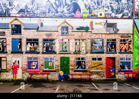 Murale artistico su una parete a Belfast, raffigurante una fila di case a schiera con vista all'interno di ciascuna delle camere. Foto Stock