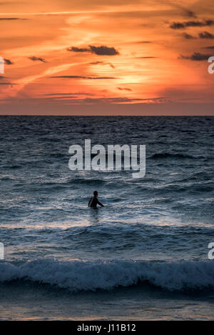 Navigare in UK. Un surfista in attesa di un'onda al tramonto, Fistral Beach, Newquay Cornwall. Foto Stock