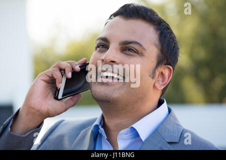 Closeup headshot ritratto, happy businessman bello in abito grigio blazer, ridendo durante la conversazione telefonica, isolata all'esterno al di fuori di sfondo Foto Stock