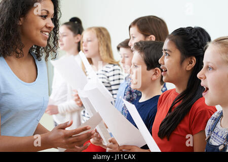 I bambini in coro scolastico essendo incoraggiati dall'insegnante Foto Stock