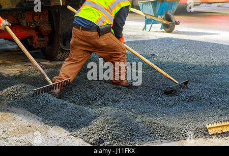 Gli uomini al lavoro, strada urbana in costruzione, asfaltatura in corso, lavoratori installare tombino fognario Foto Stock