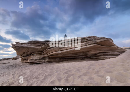 Grande roccia arenaria sulla spiaggia di Capo Trafalgar. Con il faro di Trafalgar in aggetto. Costa de la Luz, Cadice, Spagna. Foto Stock