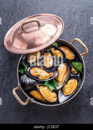 Bollito di cozze in padella di rame su sfondo di grafite. Foto Stock