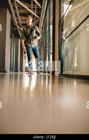 A piena lunghezza shot del giovane uomo skateboarding in ufficio. Imprenditore Casual pattinaggio attraverso office corridoio. Foto Stock