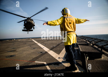 Nostromi Mate 2a classe Brynn Proudfoot, da Houston, Mn., ora dislocate sul Museo della Portaerei U.S.S. Harper's Ferry (LSD-49), U.S. Navy, segnali per un UH-60 Blackhawk gestita da una società, 3° Battaglione, 142th elicottero d'assalto battaglione, 42nd combattere la Brigata Aerea, a sbarcare su Harper's Ferry durante un ponte di atterraggio sulla qualificazione dic. 26, 2013, in qualche parte del Golfo Arabico. Stati Uniti Aviazione esercito di attività e stati uniti Navy condotta joint-service (litorale vicino a riva) missioni di formazione per costruire la familiarità con ogni altro di attrezzature e procedure tra cui lo sbarco di differenti modelli di ala rotante un Foto Stock