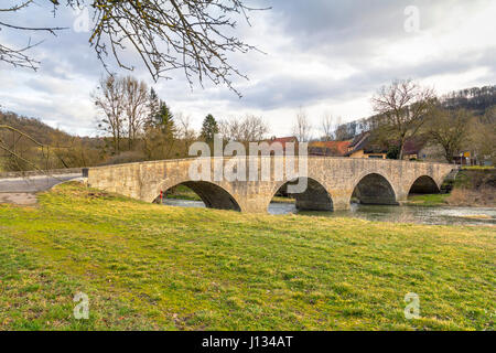 Ponte storico in pietra in un piccolo borgo rurale denominato Oberregenbach vicino a Langenburg in Hohenlohe, una zona della Germania meridionale Foto Stock