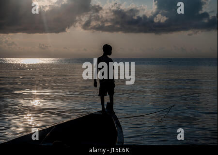 Un giovane ragazzo si erge sulla prua di una barca ormeggiata nel Lago Malawi Foto Stock