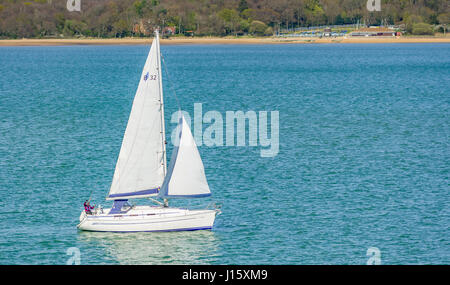Di piccole dimensioni e di colore bianco yacht. Piccolo yacht con vele di barca a vela su uno stretto tratto di acqua vicino al mare Solent, con la terra che mostra dietro lo yacht. Foto Stock