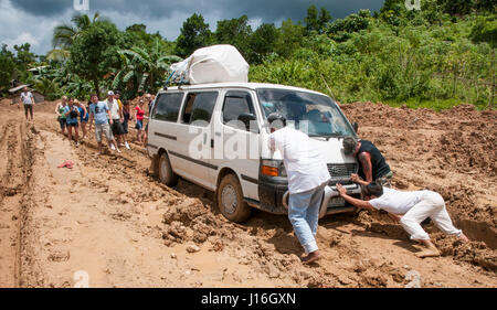 I turisti in cerca di persone locali spingendo il mini bus bloccato fuori del fango in El Nido, Palawan Foto Stock
