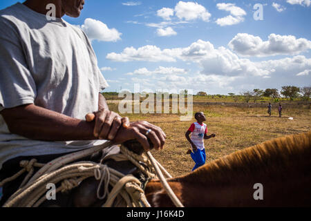 Un vecchio uomo si siede sulla parte superiore di un cavallo in primo piano mentre un ragazzo in esecuzione in Arcade Style campo da Baseball sotto un cielo sereno Foto Stock