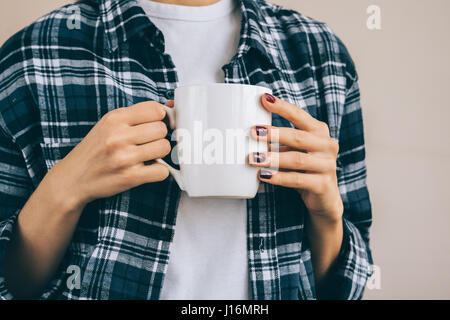 Immagine ritagliata di una donna in un plaid shirt tenendo una tazza bianca con un drink, close-up Foto Stock