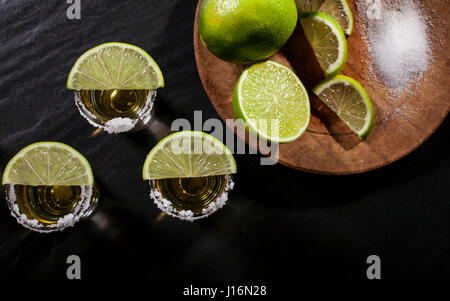 Oro tequila scatti con calce frutti su sfondo nero Foto Stock