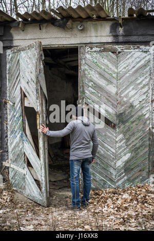 Vista posteriore di un uomo apertura deserta derlict barn Foto Stock